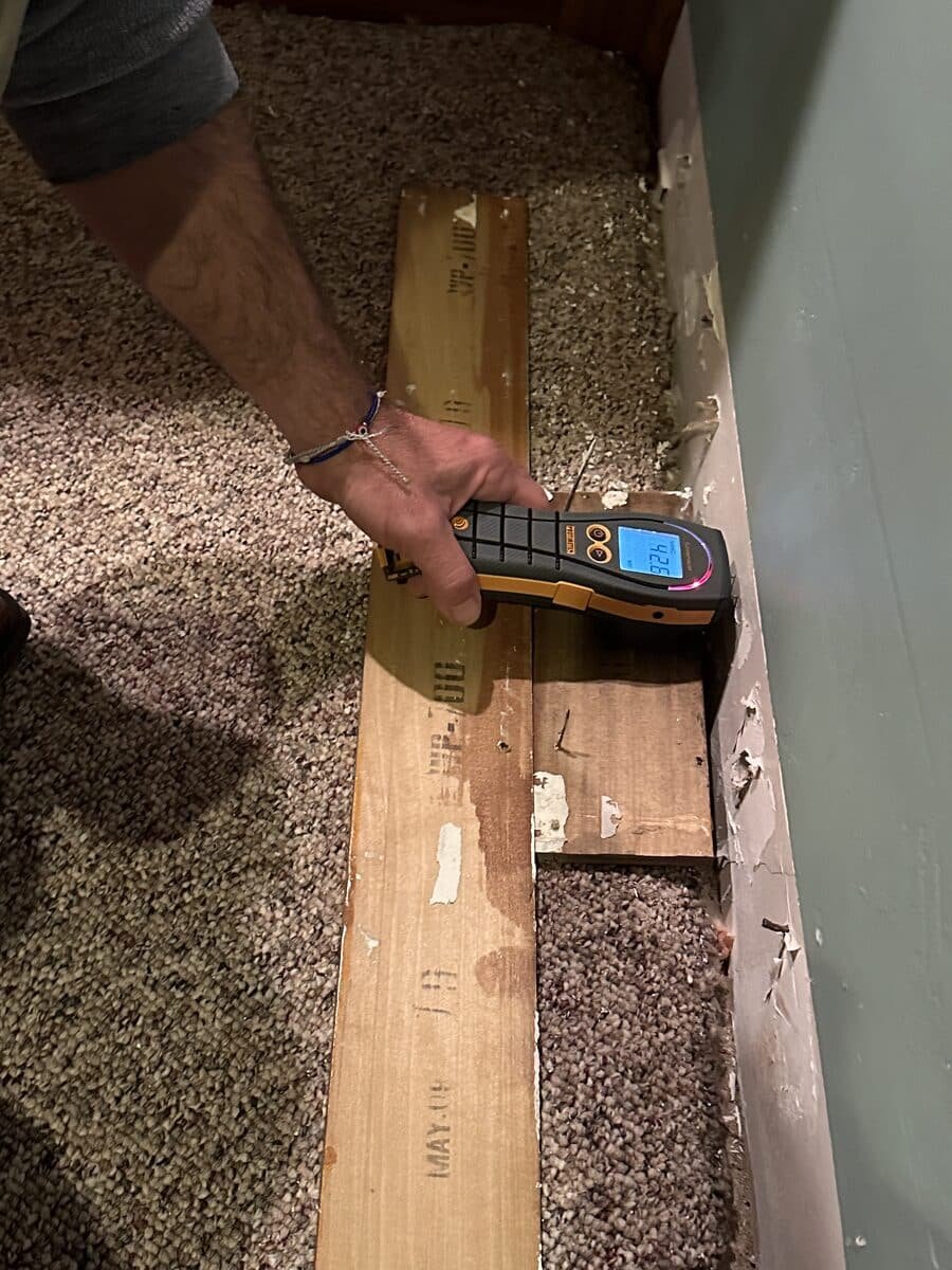 A moisture meter checking exposed material behind a removed baseboard