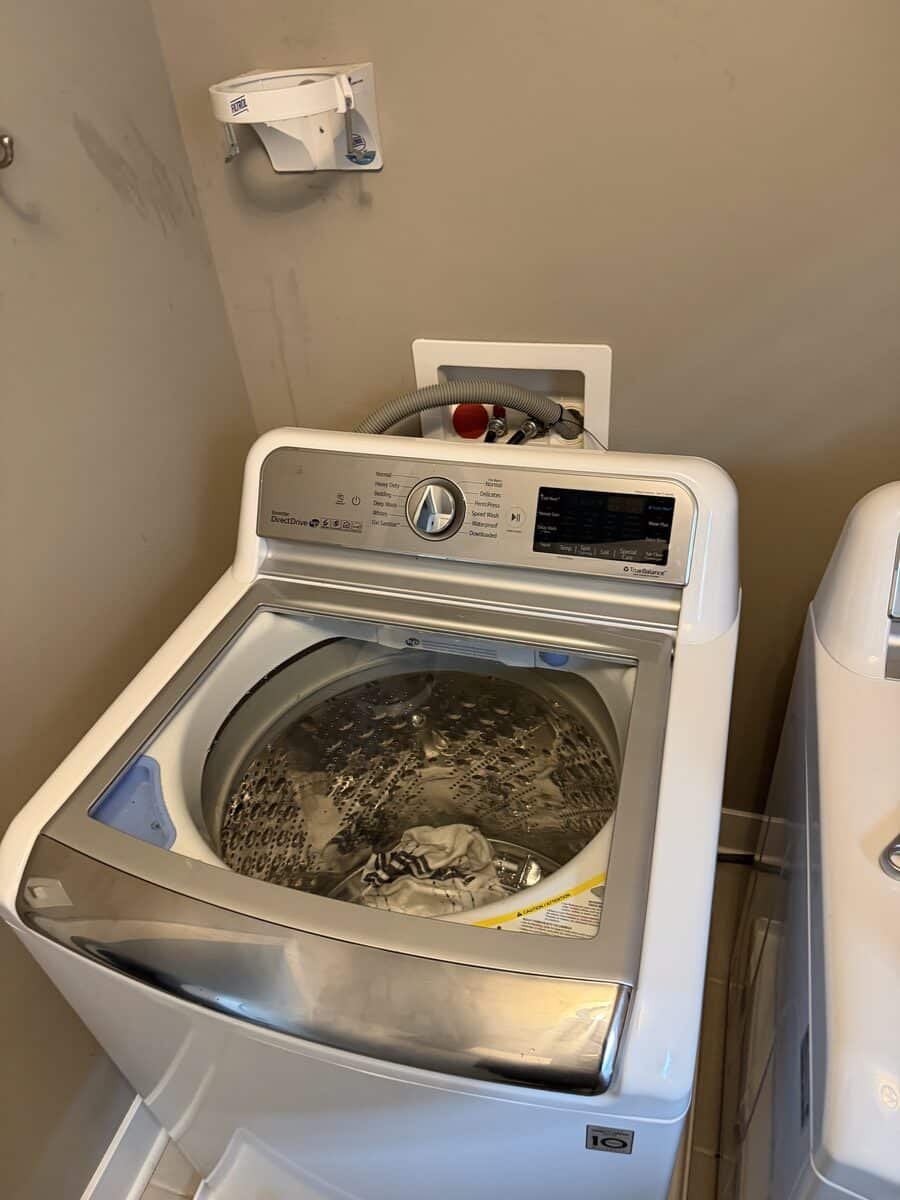 Top-loading washing machine with sudsy water and plumbing connections behind it